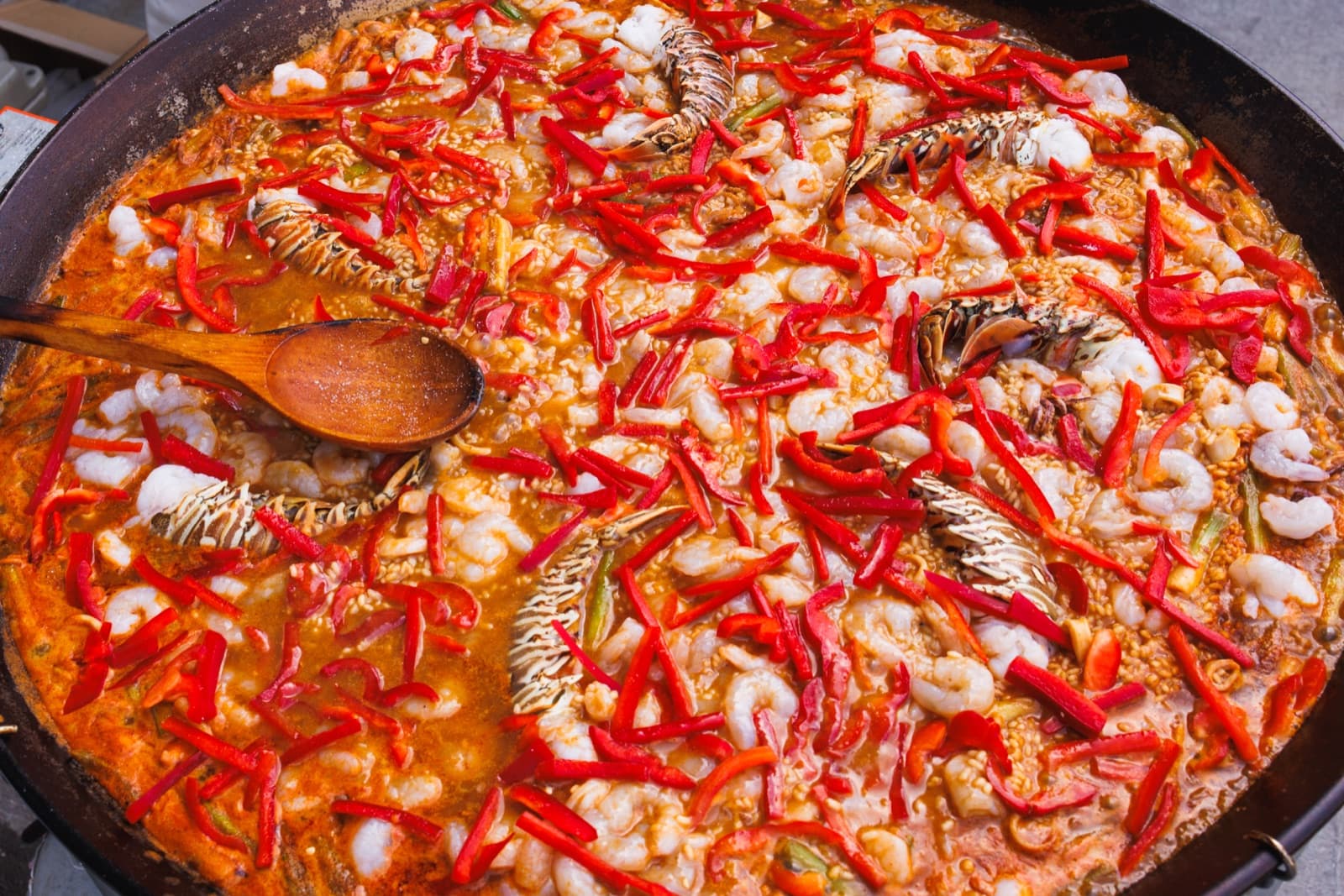Overhead view of a large seafood paella with lobster tails, shrimp, and red peppers in a wide pan