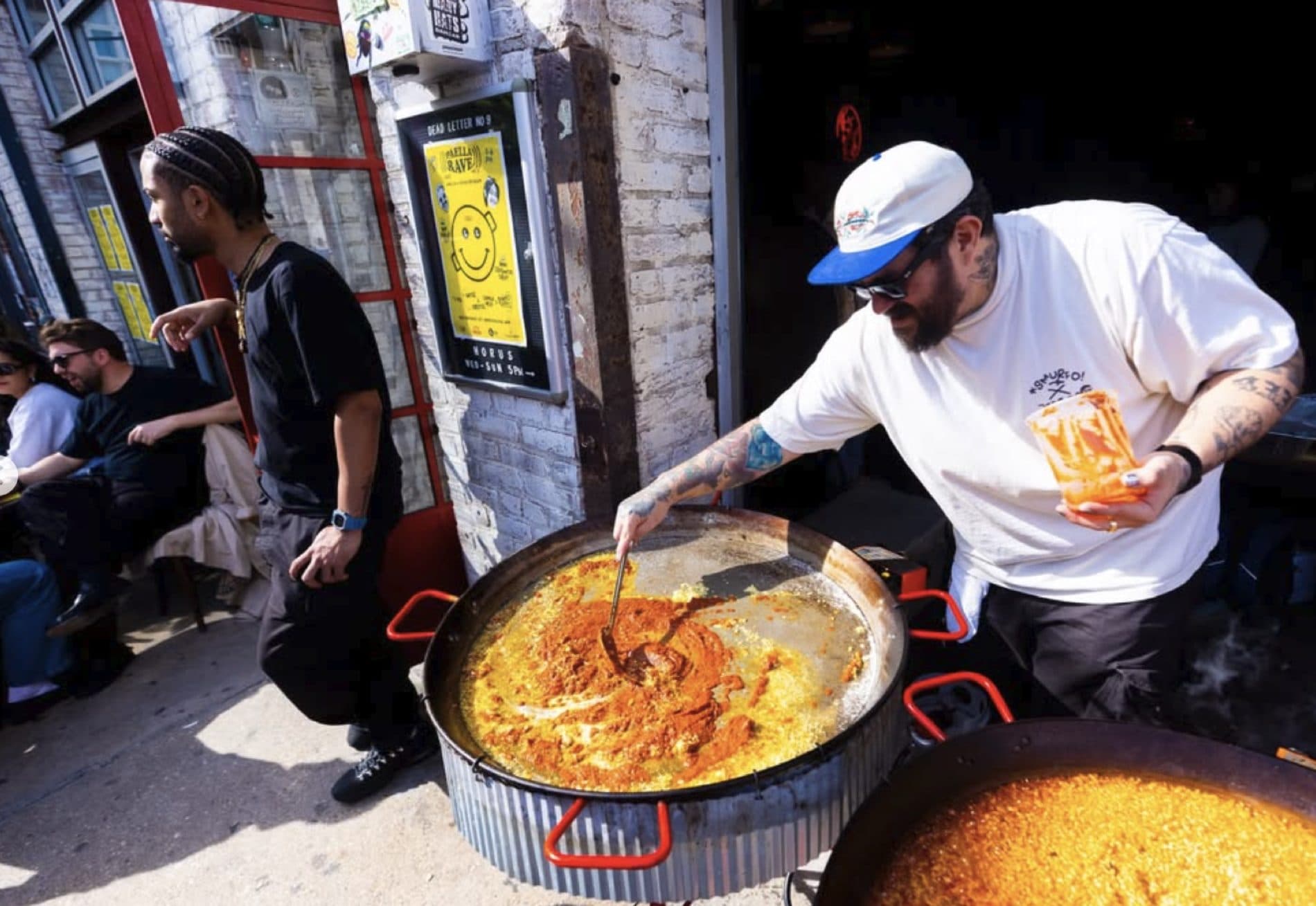 Chef Eduardo coating rice with orange sauce in a large outdoor paella pan